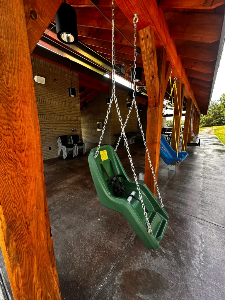 A green accessible swing hanging on the porch at Trinity Grace Farm