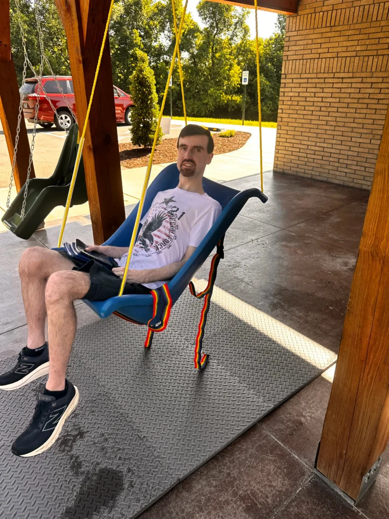 A man sits in a blue accessible swing at Trinity Grace Farm